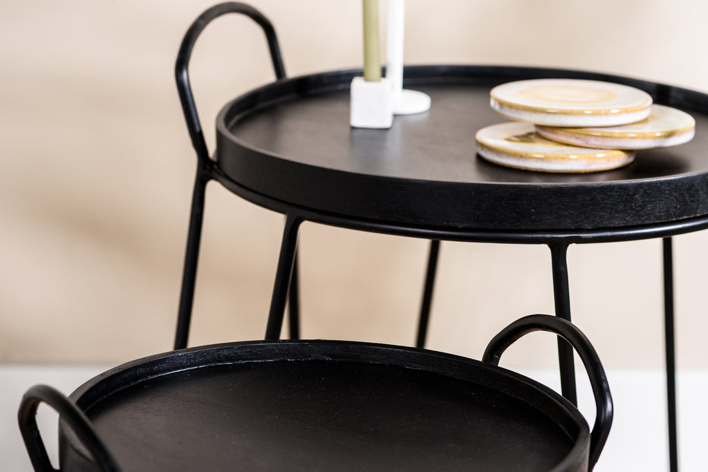 Zwarte bijzettafels met platen en kaars op een beige achtergrond, rustieke en moderne esthetiek.