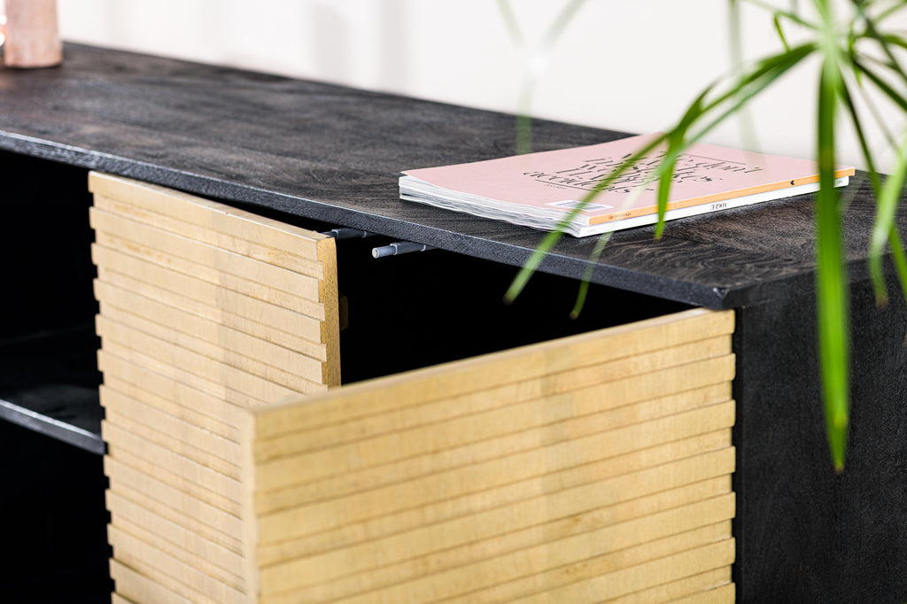 Donker houten kast met lichte houten ribbeldeur en roze tijdschrift, omlijst door groene bladeren.