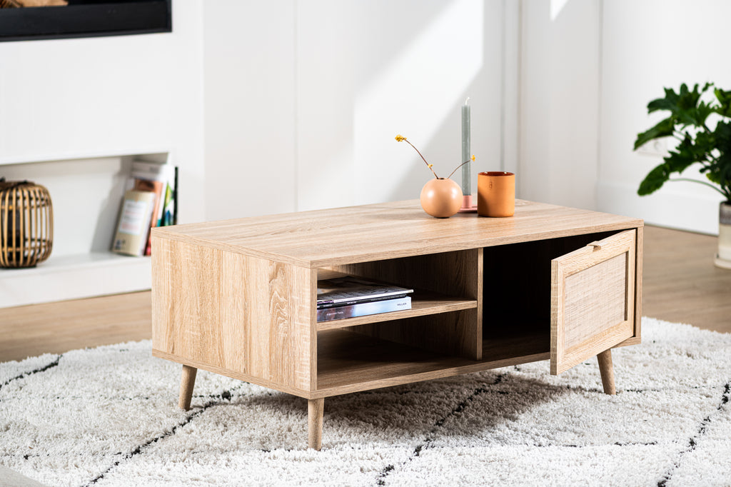 Houten salontafel met open kastdeur, versierd met vaas, kaars en boeken op een wit tapijt in een lichte woonkamer.