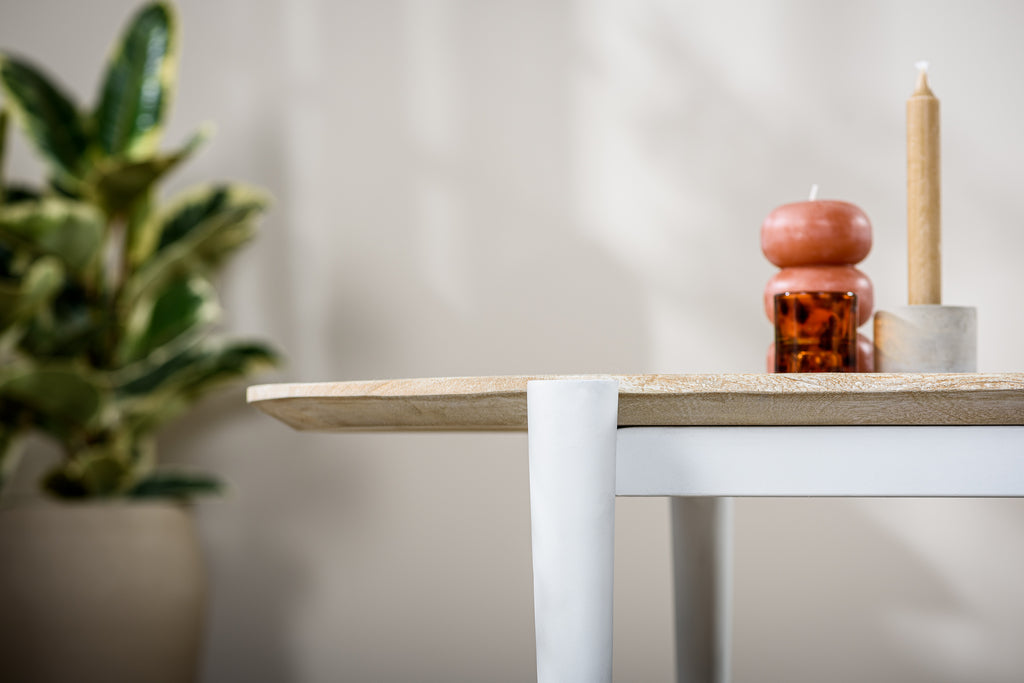 Gezellige interieurhoek met houten tafel, roze en amberkleurige kaarsen en groene plant op de achtergrond.