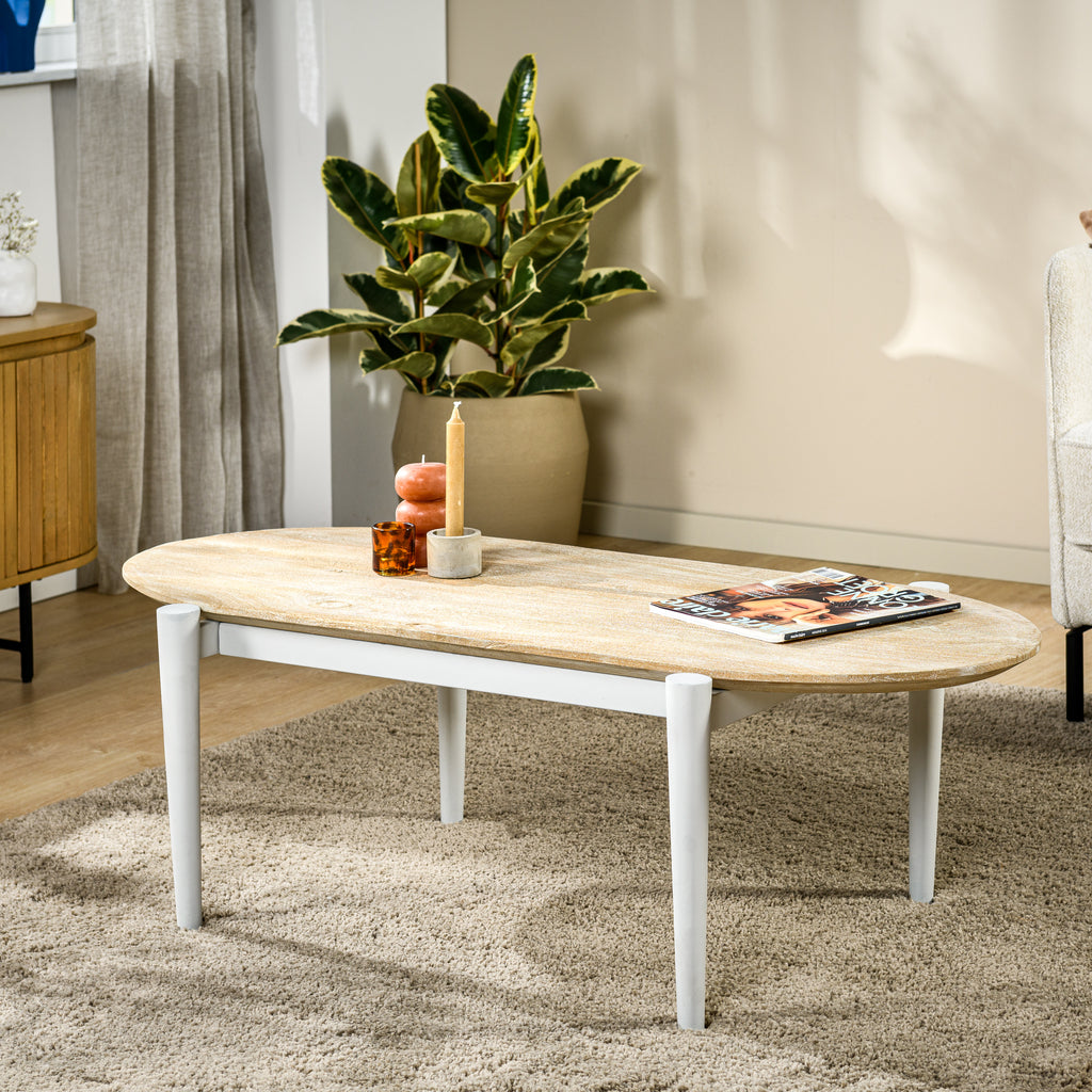 Ovale houten salontafel met kaars en tijdschriften, naast een plant op een beige tapijt in een moderne kamer.