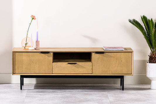 Strakke houten dressoir met zwarte poten, versierd met kaarsen, een plant en een tijdschrift in pastelkleuren.