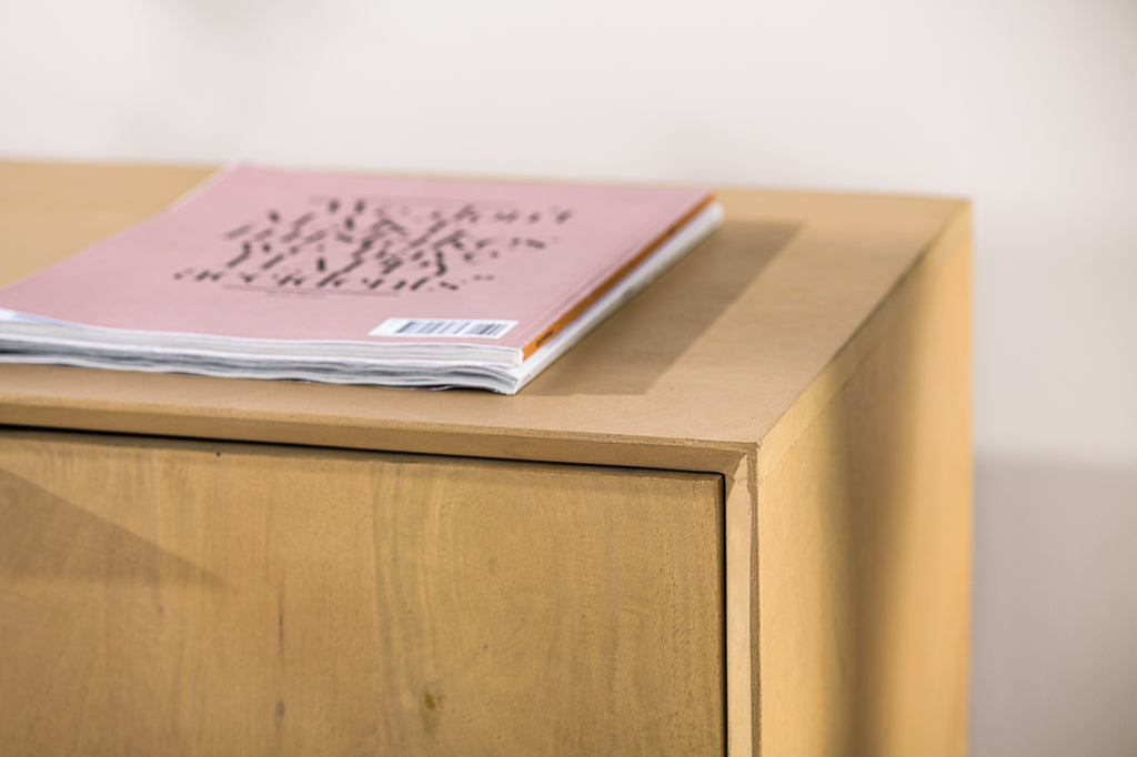 Roze tijdschrift met zwarte tekst op houten kast, minimalistische en rustige sfeer.