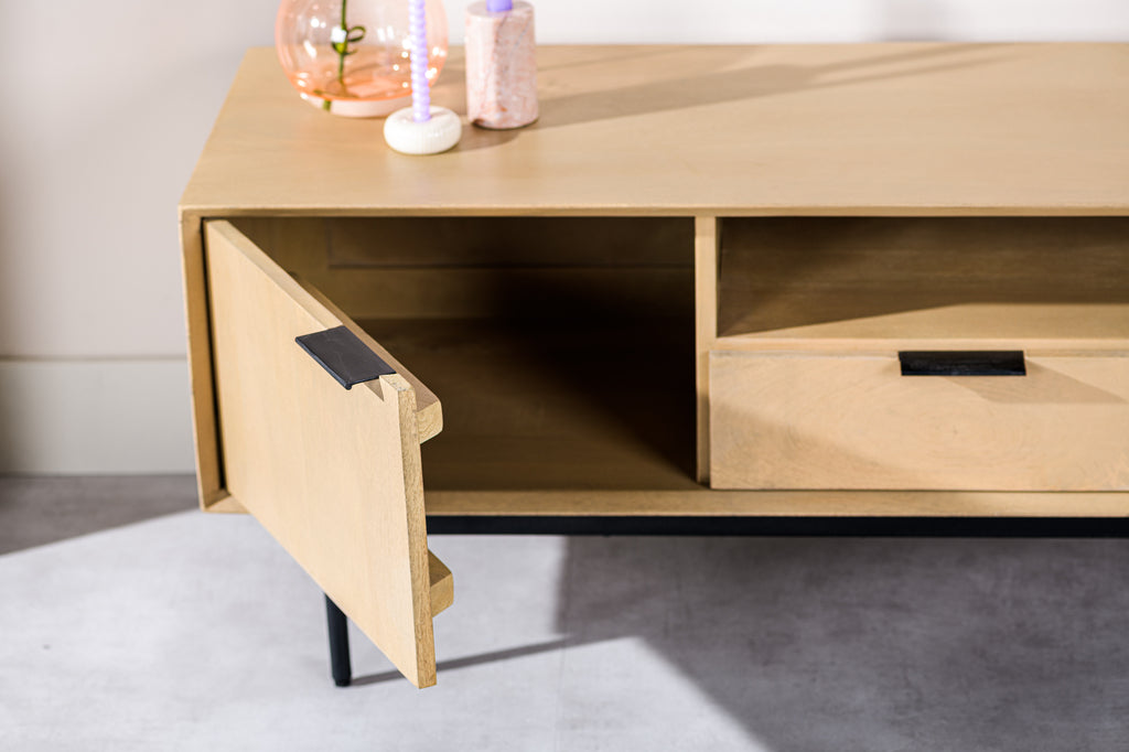 Lichte houten dressoir met geopende kastdeur, roze glaskruik en gedraaide kaarsen erbovenop.