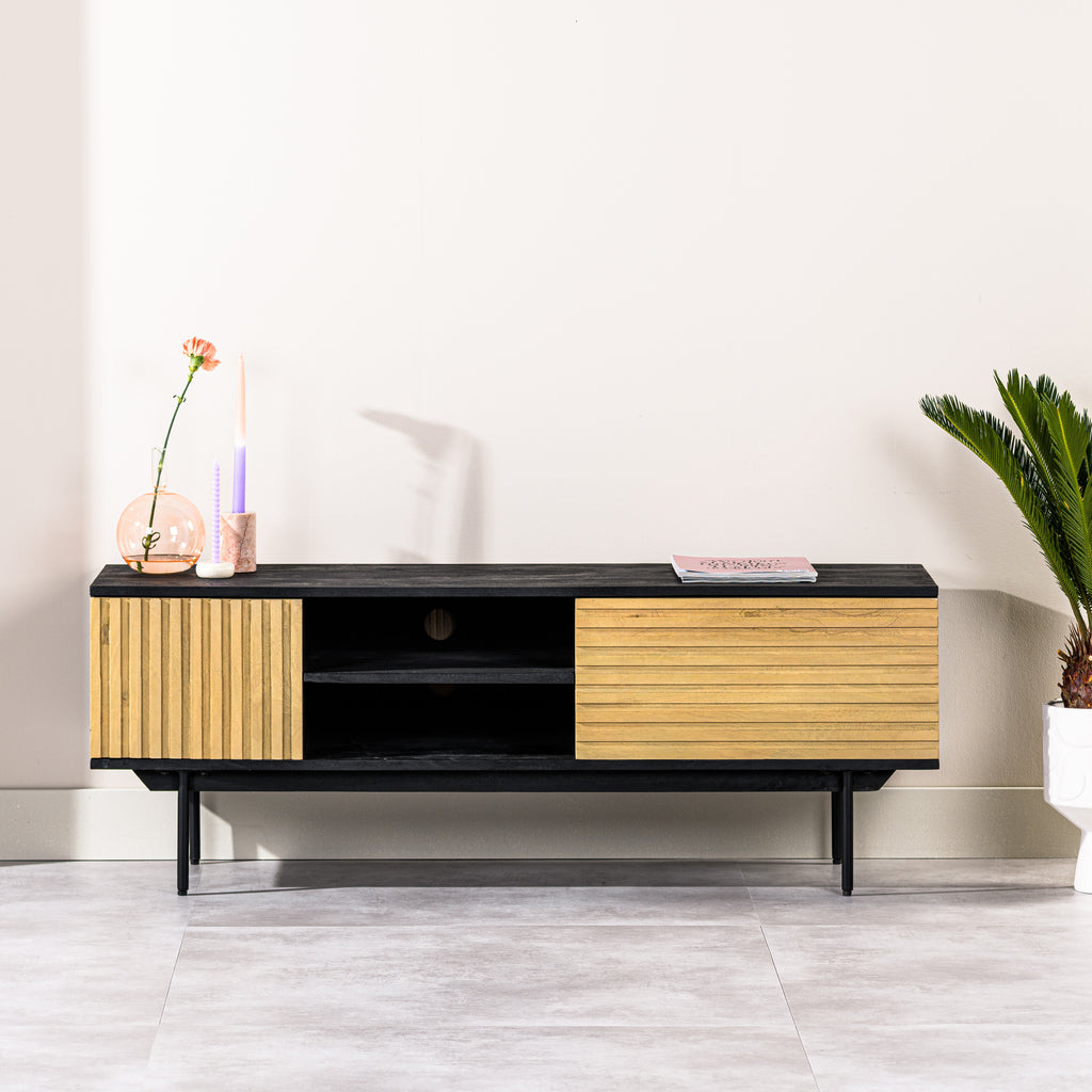 Zwart houten tv-meubel met lichte kastdeuren, oranje bloem in een vaas, kaarsen en een kleine plant rechts.