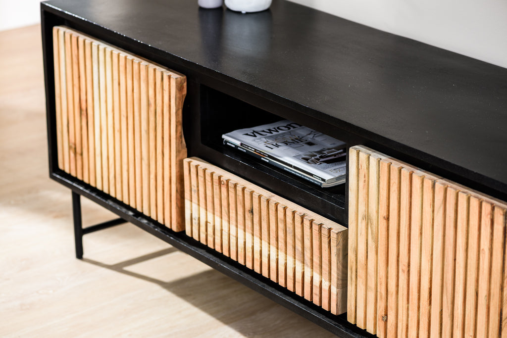 Zwart met houten tv-meubel met geribbelde deurtjes, open vak met magazines, op houten vloer.