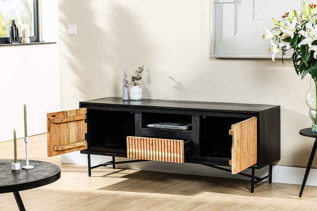 Zwart dressoir met open houten deurtjes, witte bloemen in vaas en decoratieve kaarsen op een lichte houten vloer.