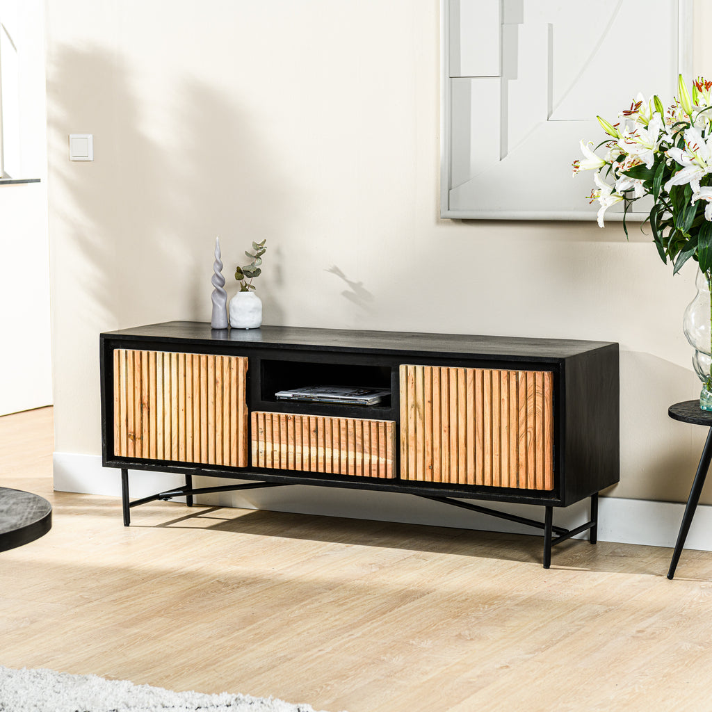 Zwart tv-meubel met ribbelhouten deuren, decoratieve vazen en bloemen op houten vloer en lichte muur.