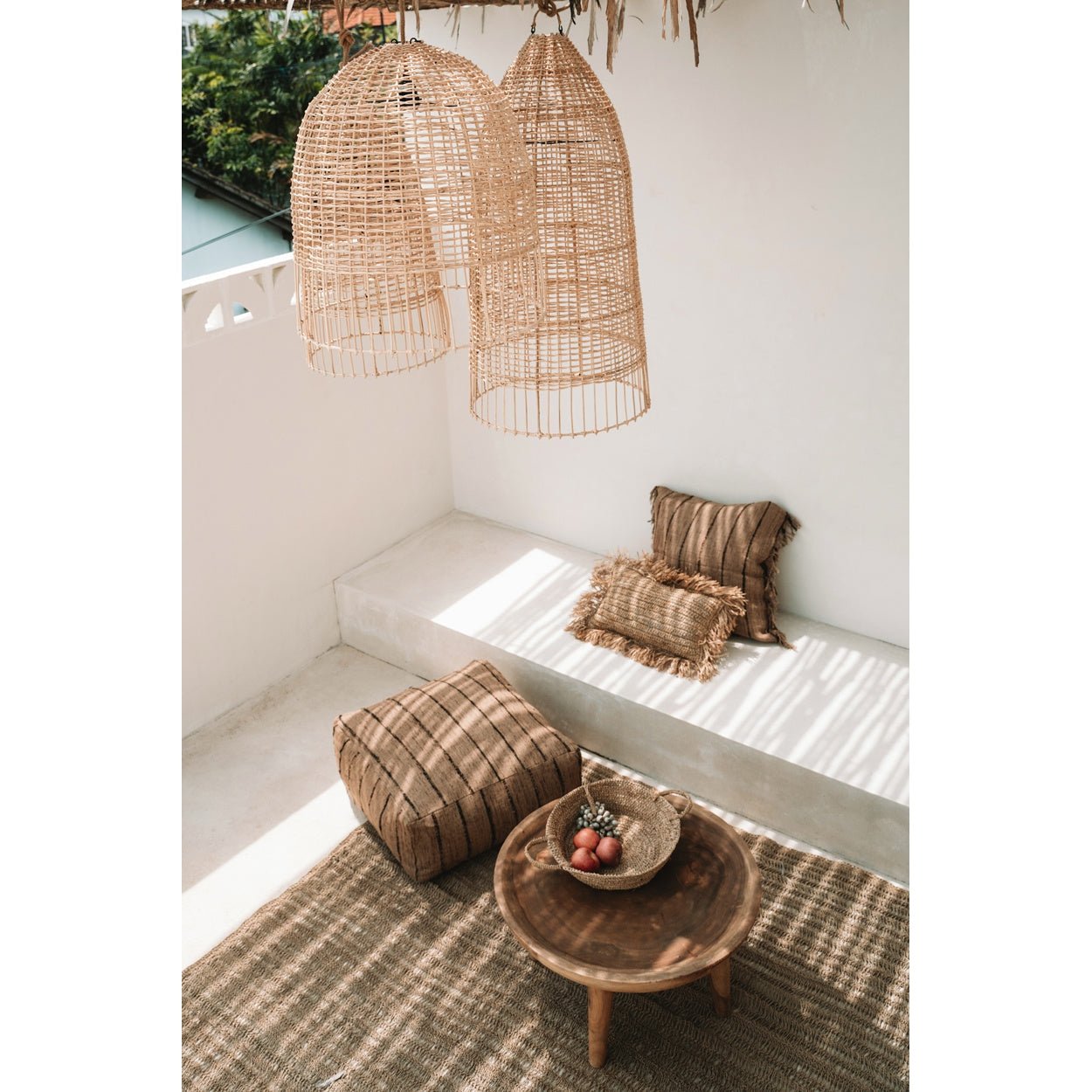 Stijlvolle zonnige patio met rotan lampen, rustieke kussens en een houten tafel met een mand vol fruit.