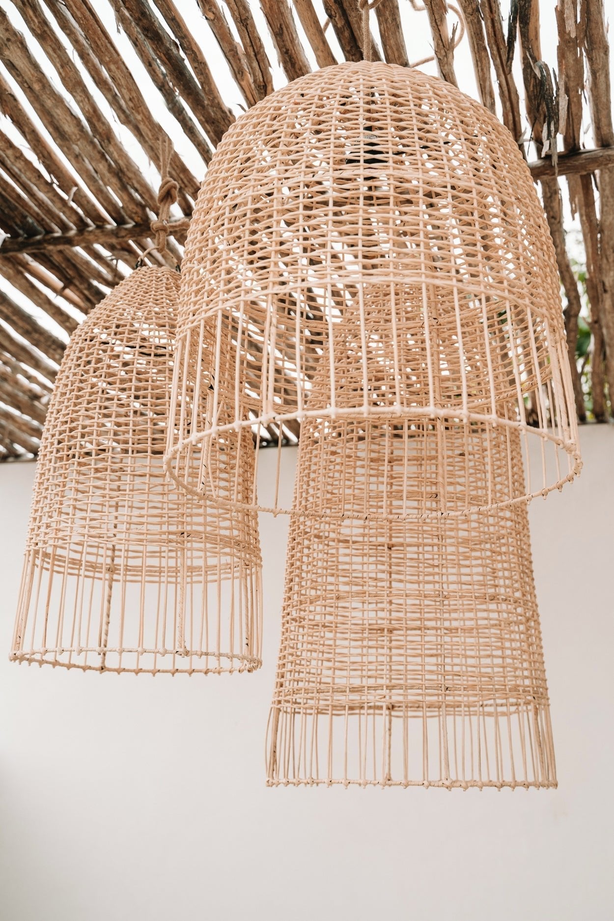 Grote, geweven rotan hanglampen onder een houten dak, zorgen voor een rustiek, natuurlijke sfeer.