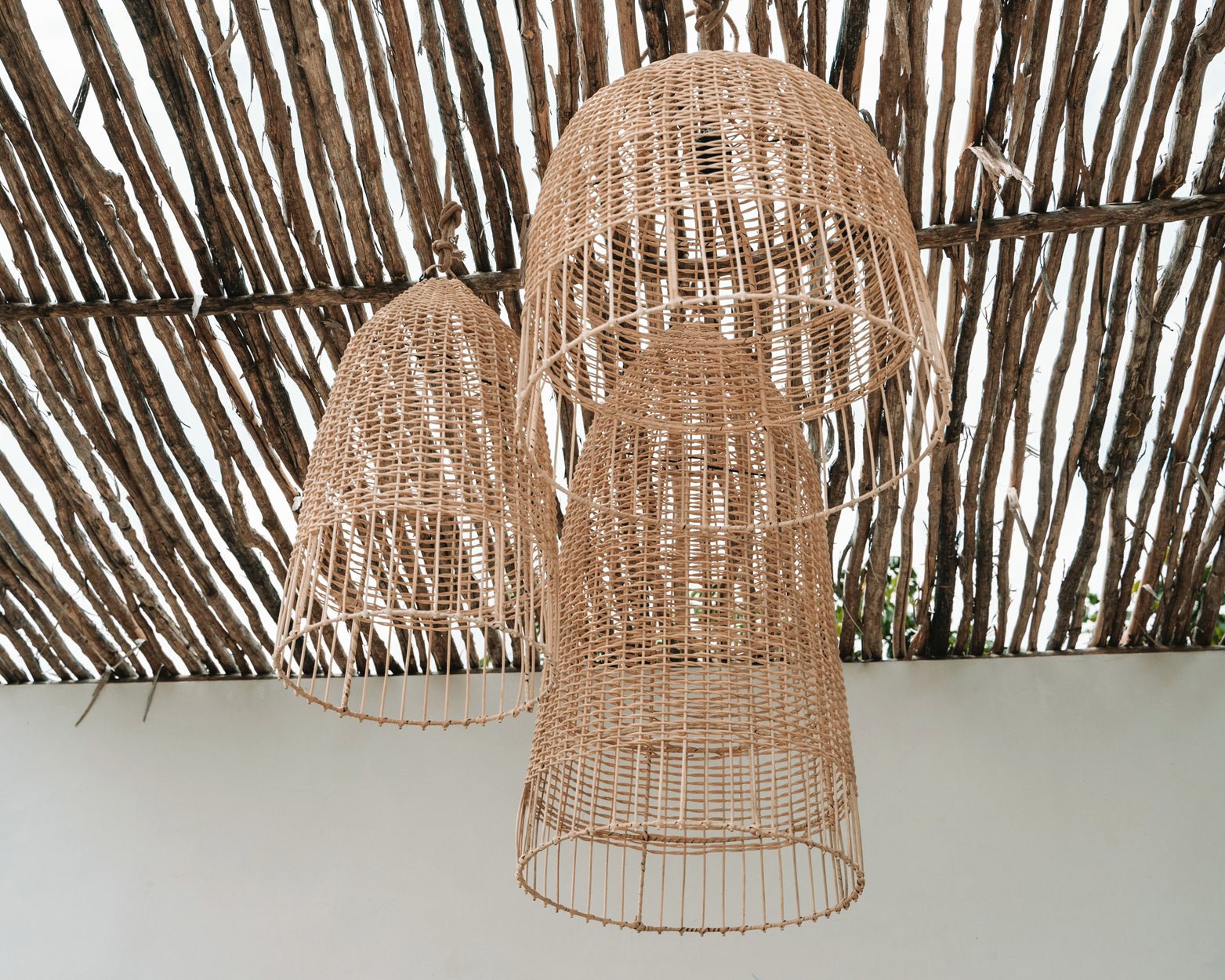 Drie bamboe lampenkappen hangen onder een houten dak, met een minimalistisch en natuurlijk ontwerp.