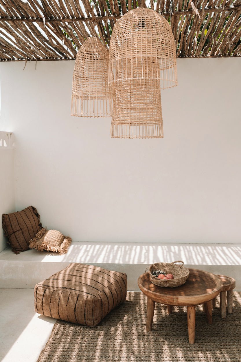 Rustieke zithoek met rotan lampen, houten meubels en kussens op een geweven tapijt, onder schaduwrijke pergola.