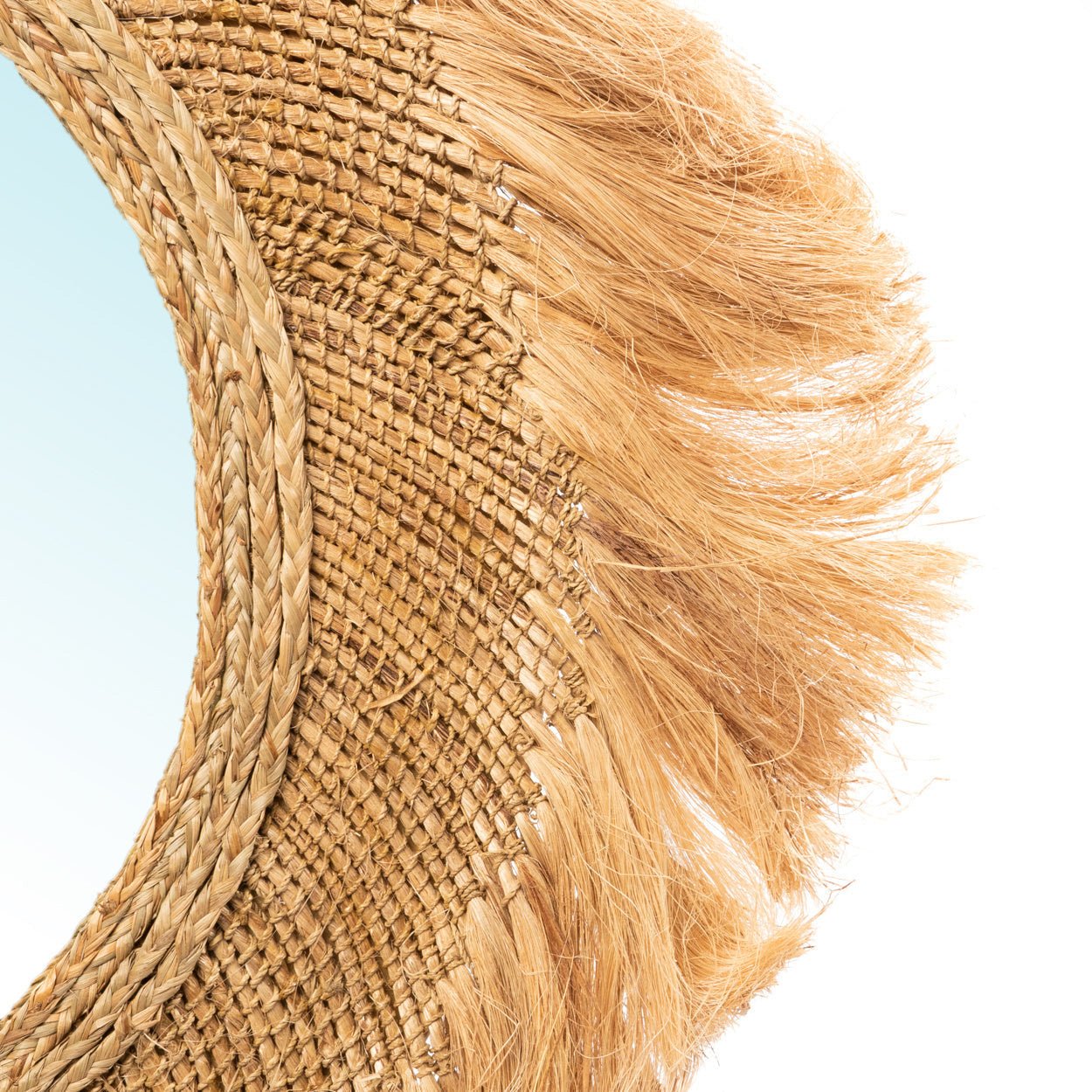 Ronde spiegel met een geweven jute omlijsting, met natuurlijke rafelige texturen op een lichtblauwe achtergrond.