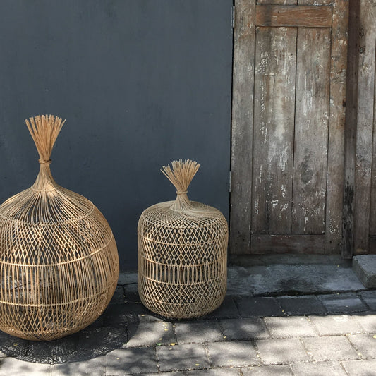 Twee decoratieve rieten manden tegen een donkere muur naast een verweerde houten deur op een zonnige dag.