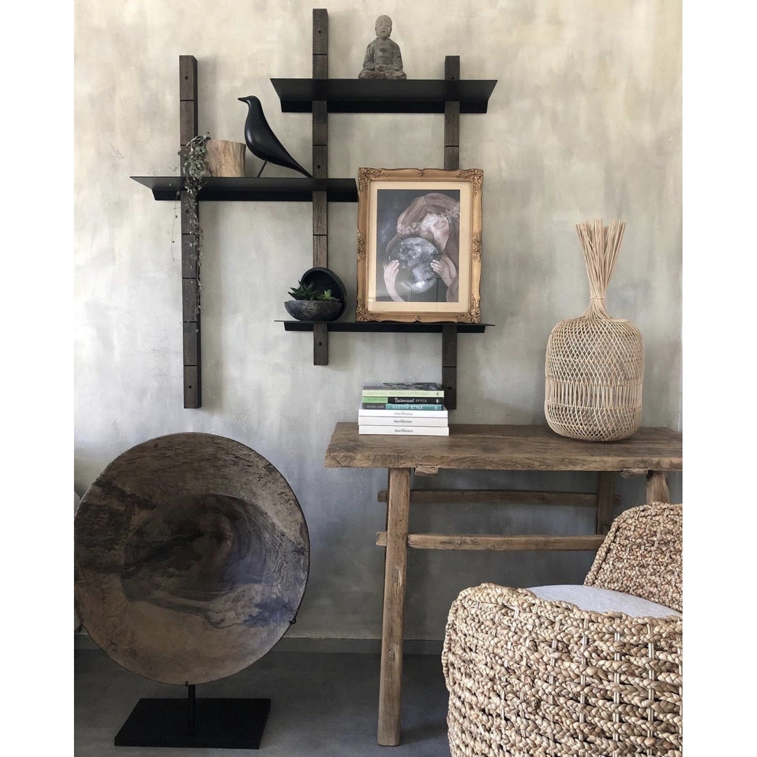 Stijlvolle woonkamerhoek met houten tafel, planken met decoraties, rieten mand en een stapel boeken.