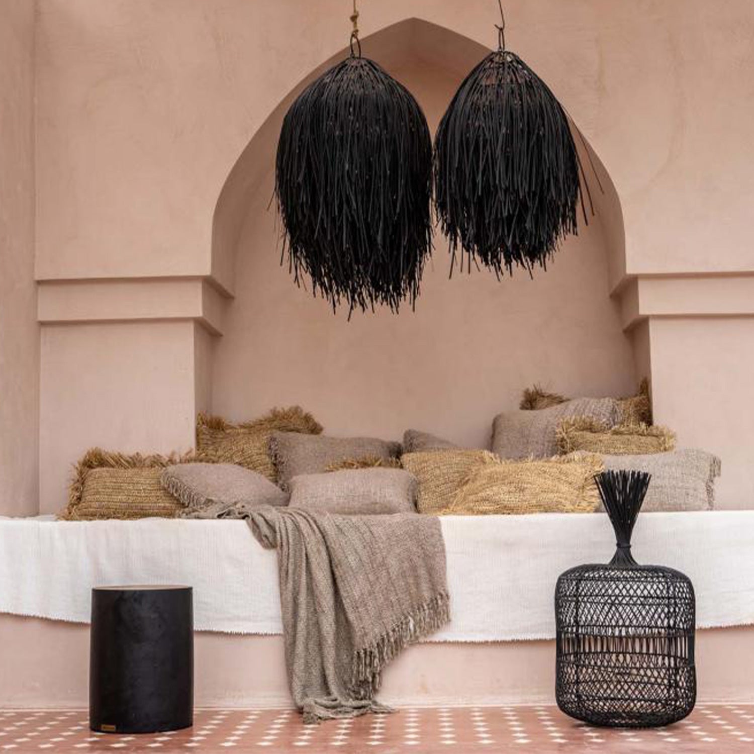 Sfeervolle zithoek met beige kussens in nis, twee zwarte hanglampen en een decoratieve mand op terracotta vloer.