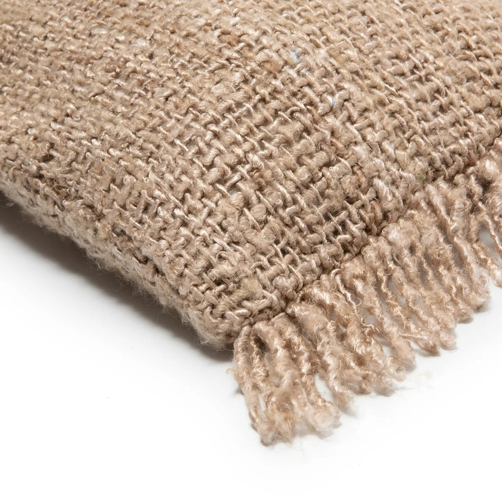 Beige geweven deken met franjes en ruwe textuur, zorgvuldig gevouwen op een witte achtergrond.