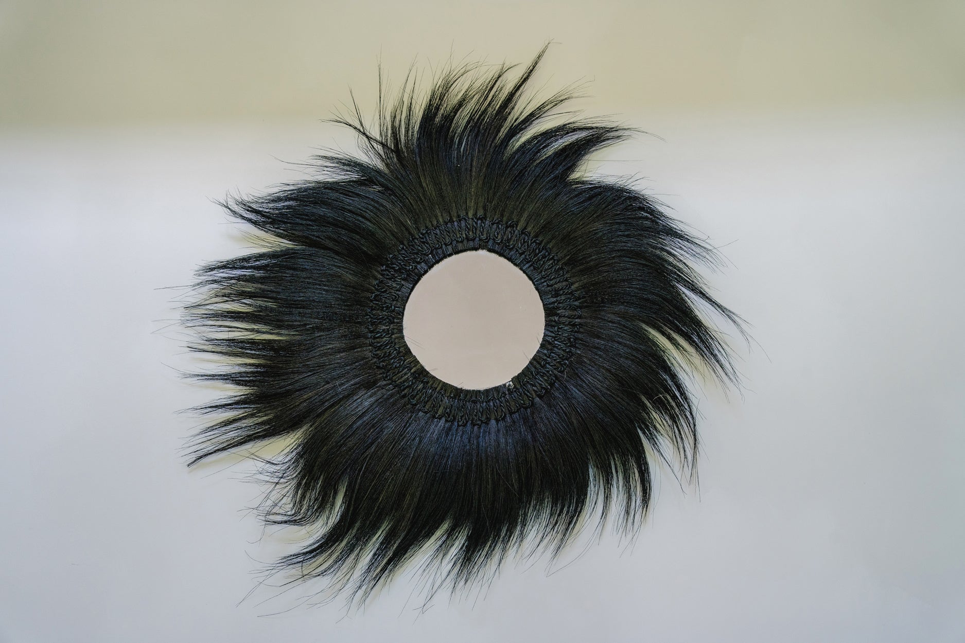 Rond kunstwerk met zwart haar dat straalt vanuit een centrale cirkel op een lichte achtergrond.