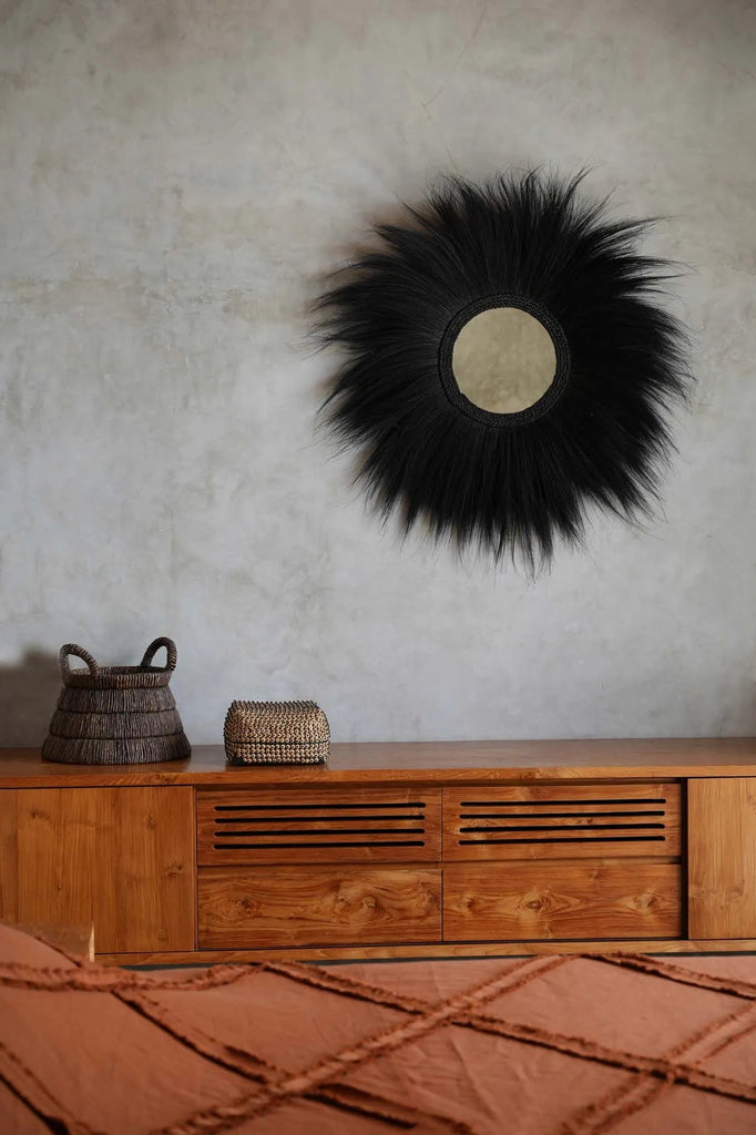 Zwarte pluizige wandspiegel boven houten dressoir met twee manden, warme aardetinten in sfeervolle kamer.