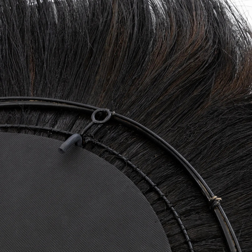 Zwart, rond borstelonderdeel met dichte haren en metalen ring, deels zichtbaar tegen een lichte achtergrond.