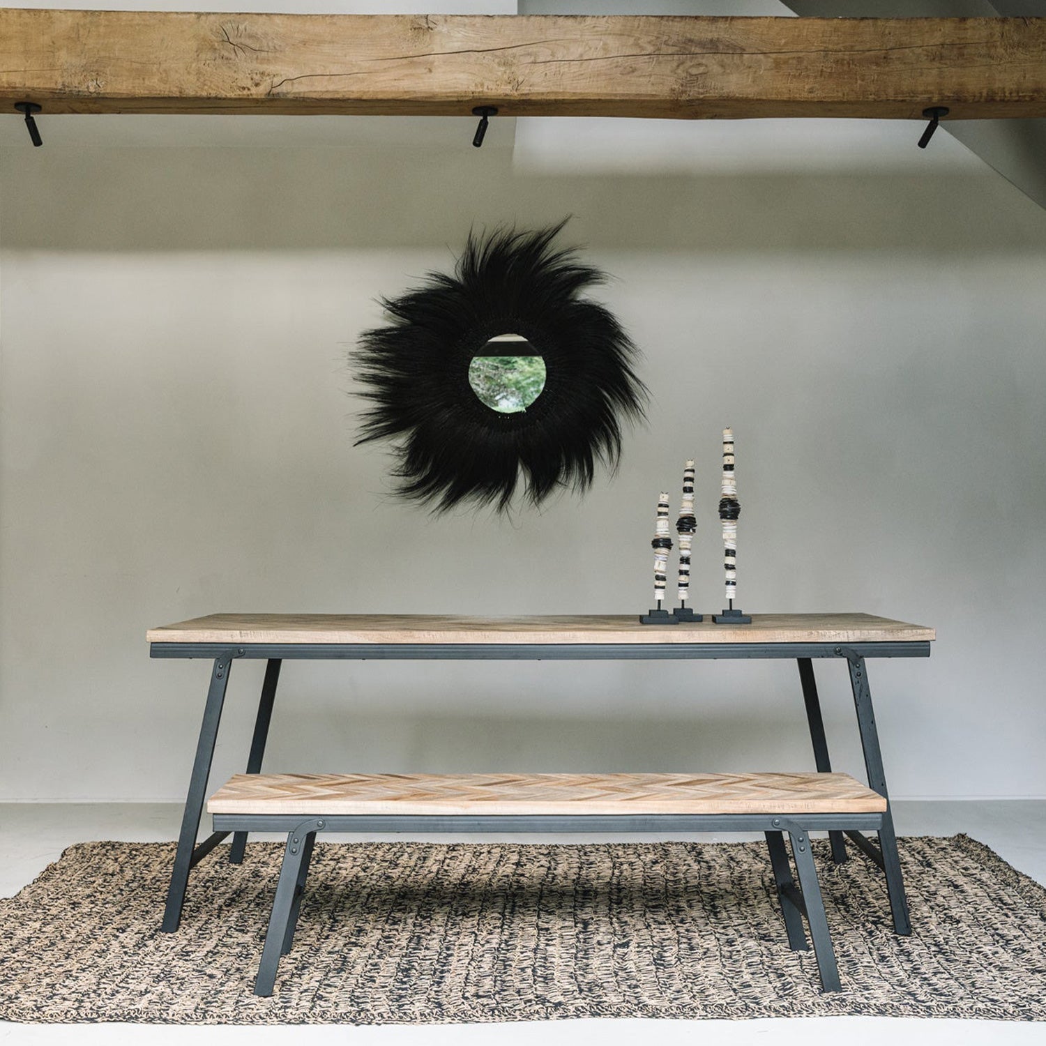 Houten tafel en bank op gevlochten tapijt, zwarte decoratieve spiegel aan de muur, minimalistische inrichting.