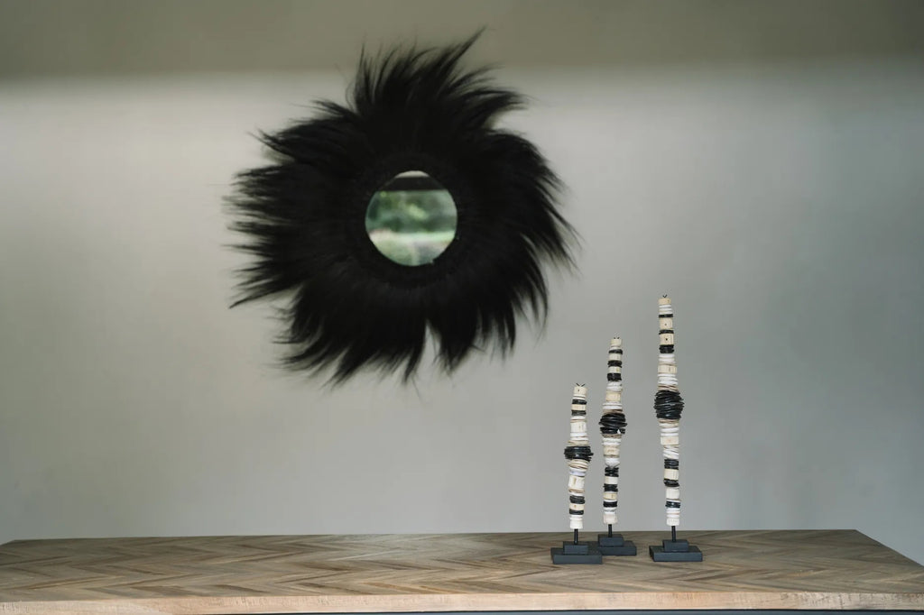Zwarte harige spiegel en moderne sculpturen op houten tafel tegen een grijze muur in minimalistisch interieur.