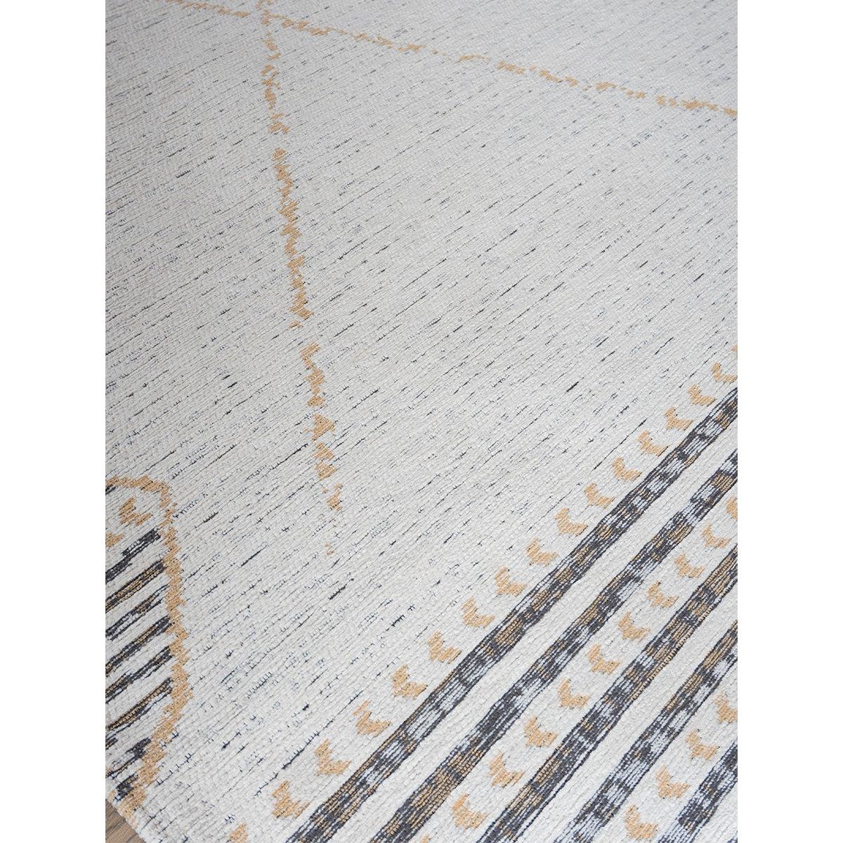 Crèmekleurig tapijt met subtiele zwarte en bruine geometrische patronen, diagonale lijnen en stippen.