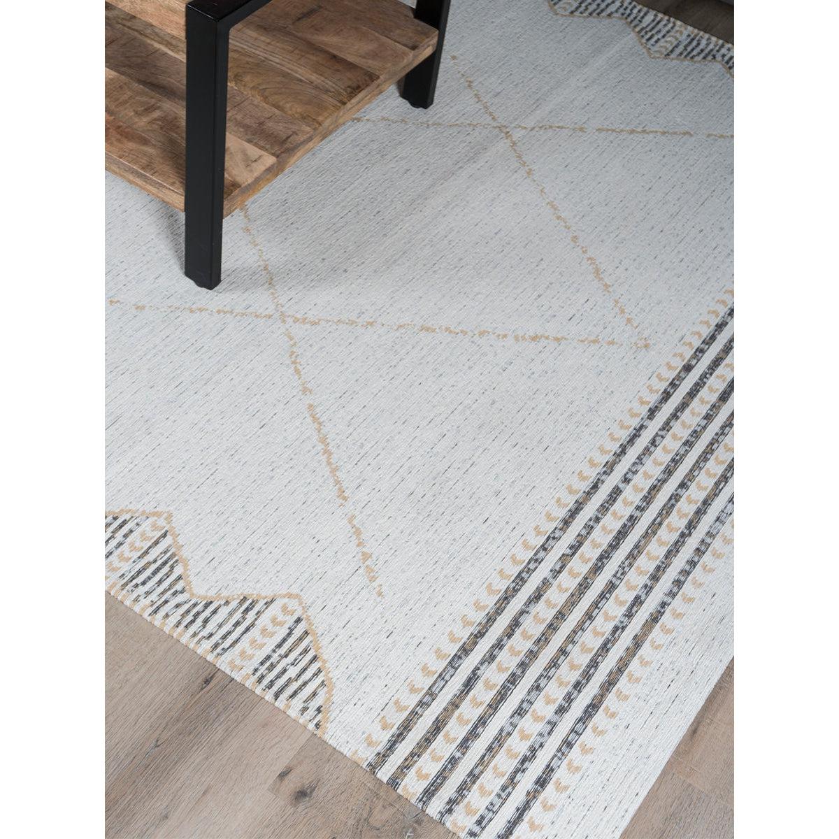 Crème tapijt met bruine en grijze geometrische patronen, naast een houten tafel op een houten vloer.