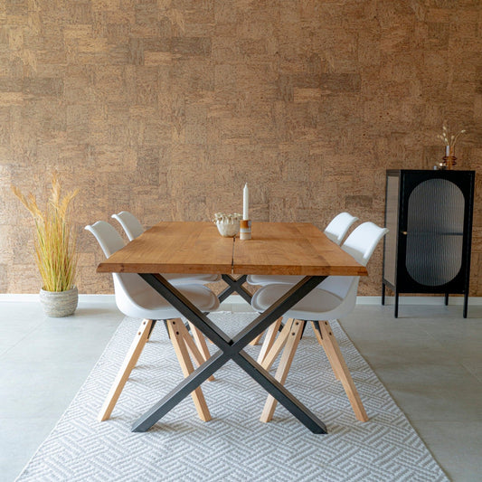 Eettafel met houten blad, vier witte stoelen, minimalistische vaas en kast tegen een warme kurkwand.