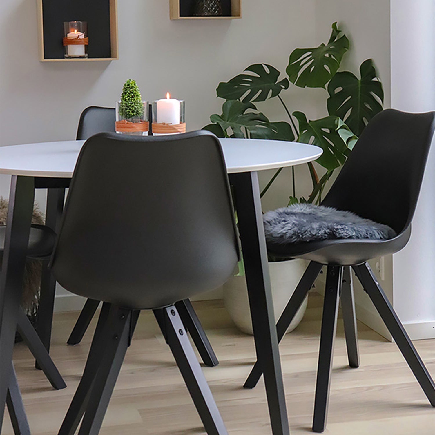 Moderne eetkamer met zwarte stoelen, wit rond tafelblad, brandende kaars, planten en houten vloer.