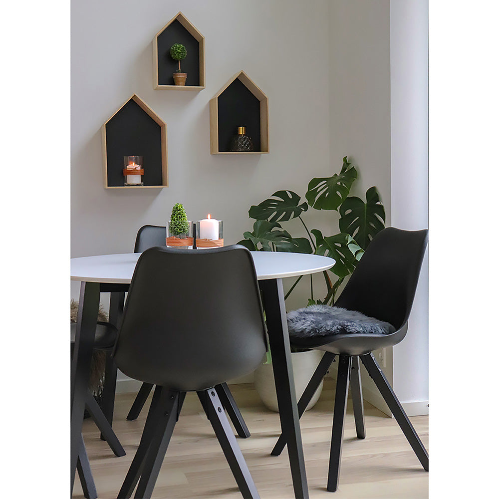 Moderne eetkamer met ronde tafel, zwarte stoelen, groene kamerplant en wandplanken met decoraties.