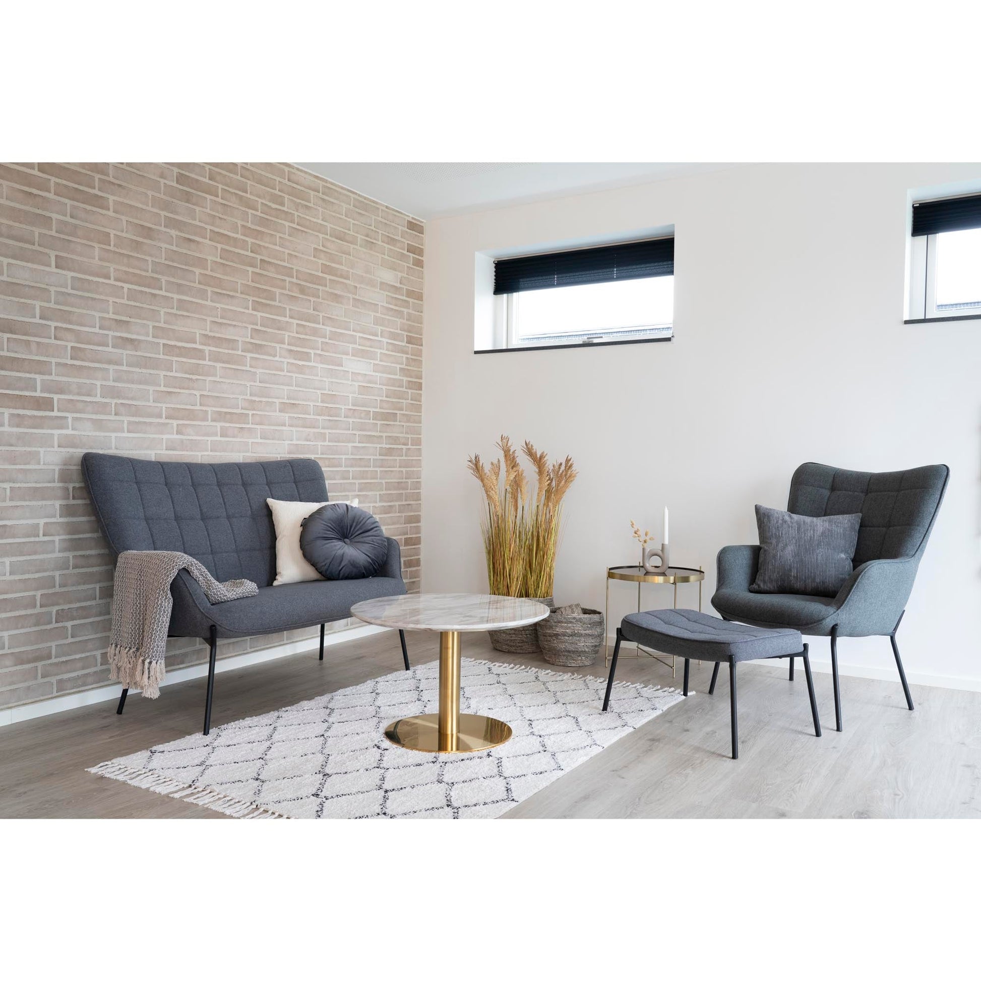 Moderne woonkamer met grijze bank, fauteuil en bijzettafel. Licht houten vloer en beige bakstenen muur.