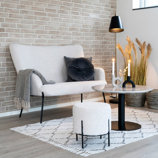 Stijlvolle zithoek met beige bank, donkere kussens, een kleine tafel, vloerkleed en zachte verlichting.