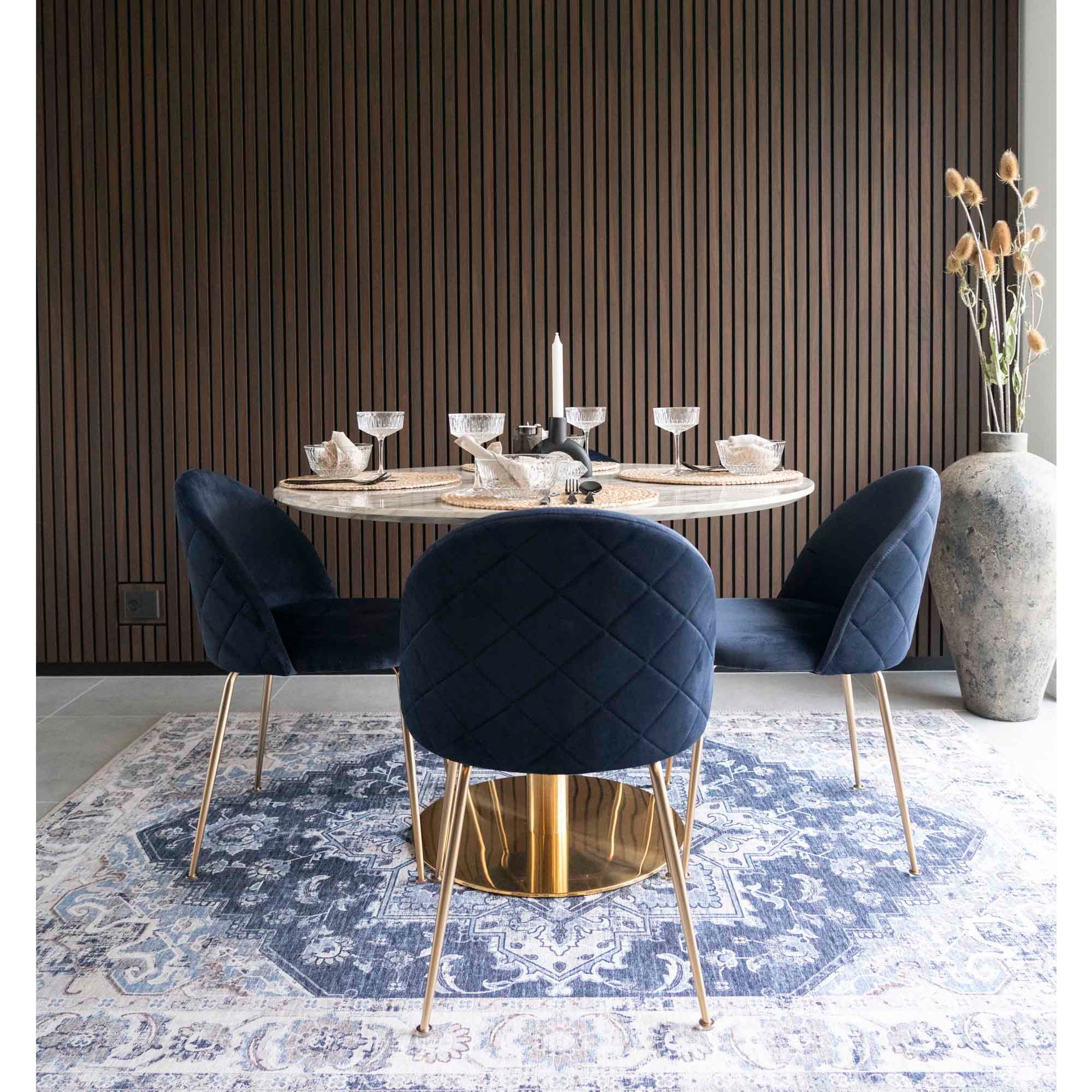 Elegante eetkamer met blauwe fluwelen stoelen rond een gedekte tafel op een Perzisch tapijt, bruine wand.