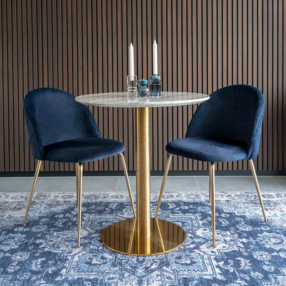Ronde marmeren tafel met gouden poot, omringd door donkerblauwe stoelen, op een gedetailleerd blauw tapijt.