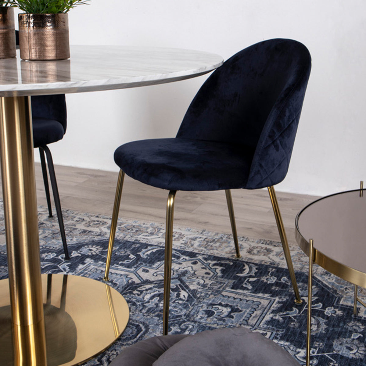 Donkerblauwe stoel met gouden poten bij marmeren tafel, op een luxe blauw-wit patroon tapijt.