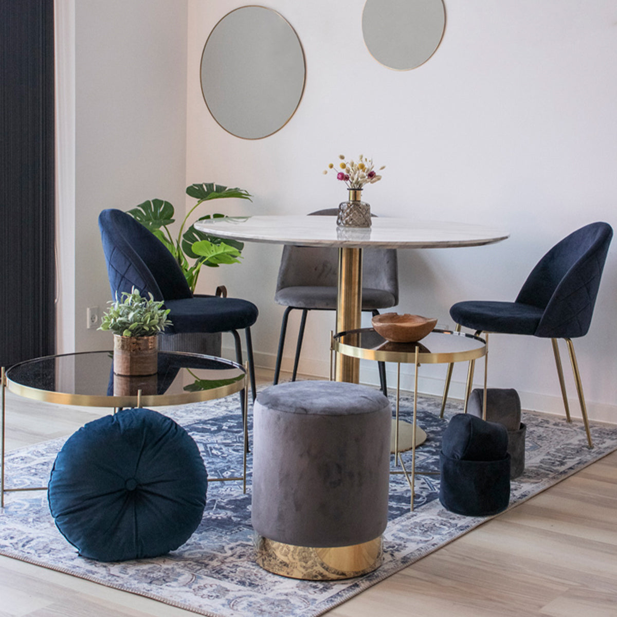 Stijlvolle eetkamer met ronde tafel, fluwelen stoelen, planten en ronde spiegels aan een witte muur.