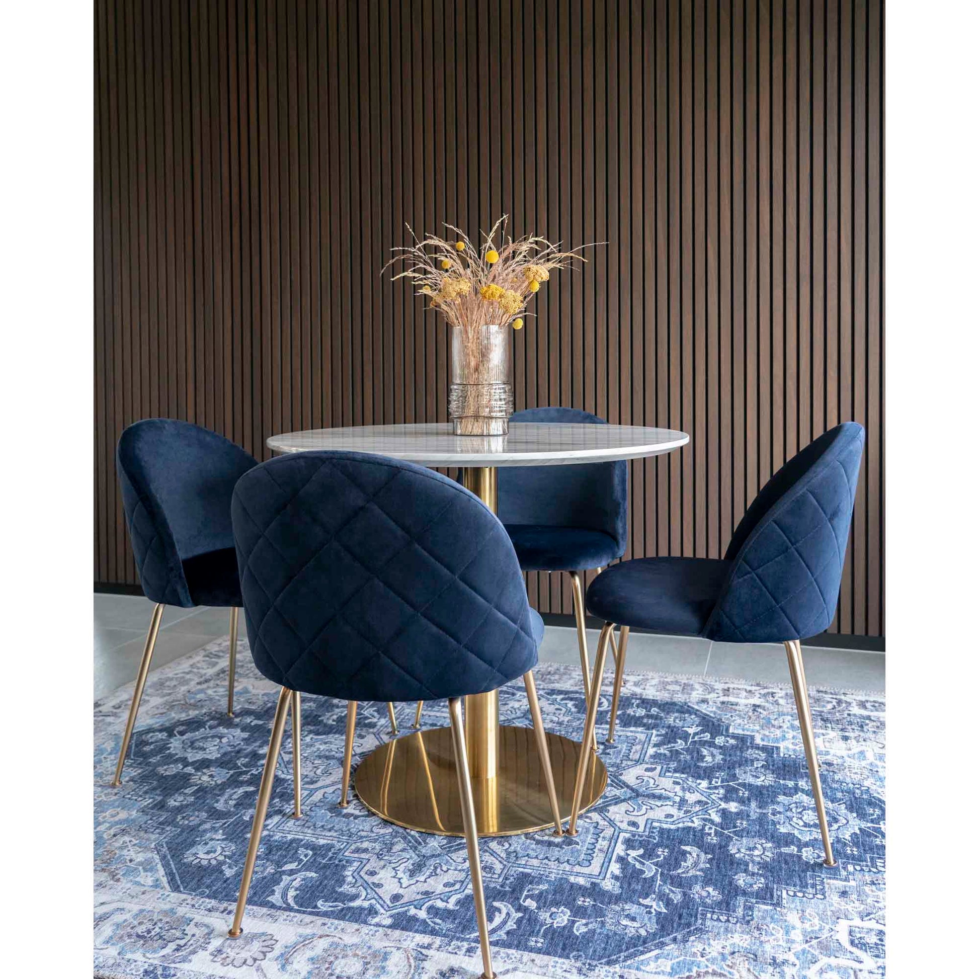 Elegante eethoek met een rond marmeren tafelblad, vier blauwe stoelen op een vintage blauw tapijt.