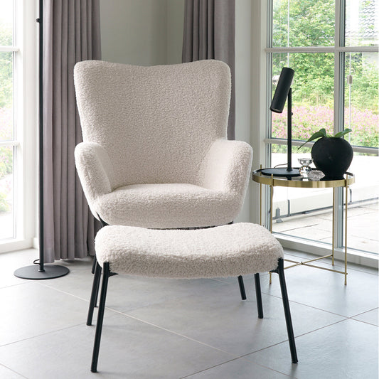 Gezellige woonkamer met zachte, witte fauteuil en bijpassende poef, naast een gouden bijzettafel met plant.