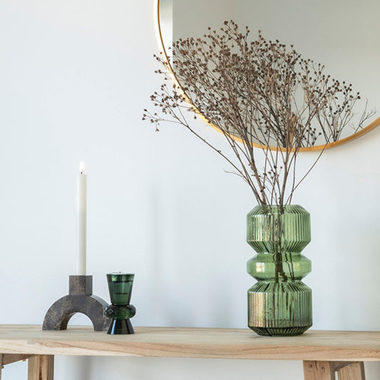 Stijlvolle houten tafel met groene glazen vaas met droogbloemen, brandende kaars en moderne spiegel.