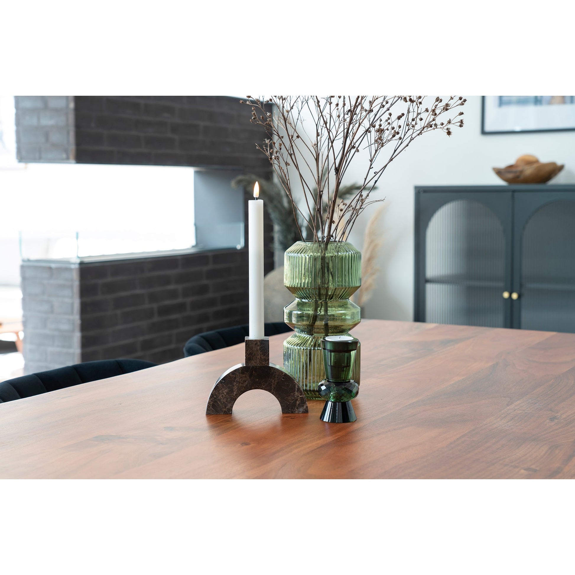 Moderne houten tafel met groene glazen vazen en brandende kaars in sierlijke kandelaar, sfeervol interieur.