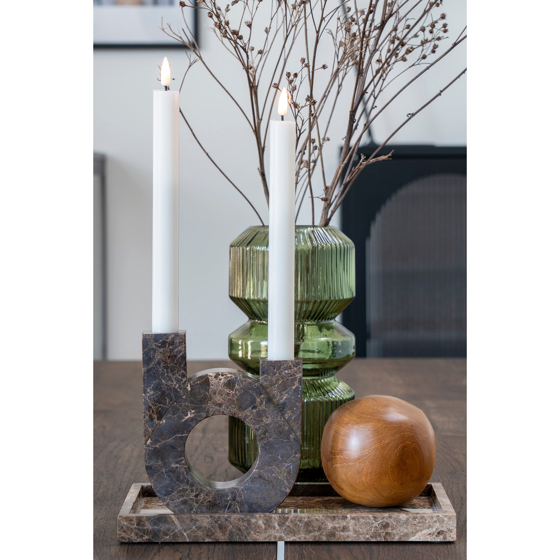 Witte kaarsen in marmeren kandelaar met groene vaas en droogbloemen op een houten tafel, rustieke sfeer.