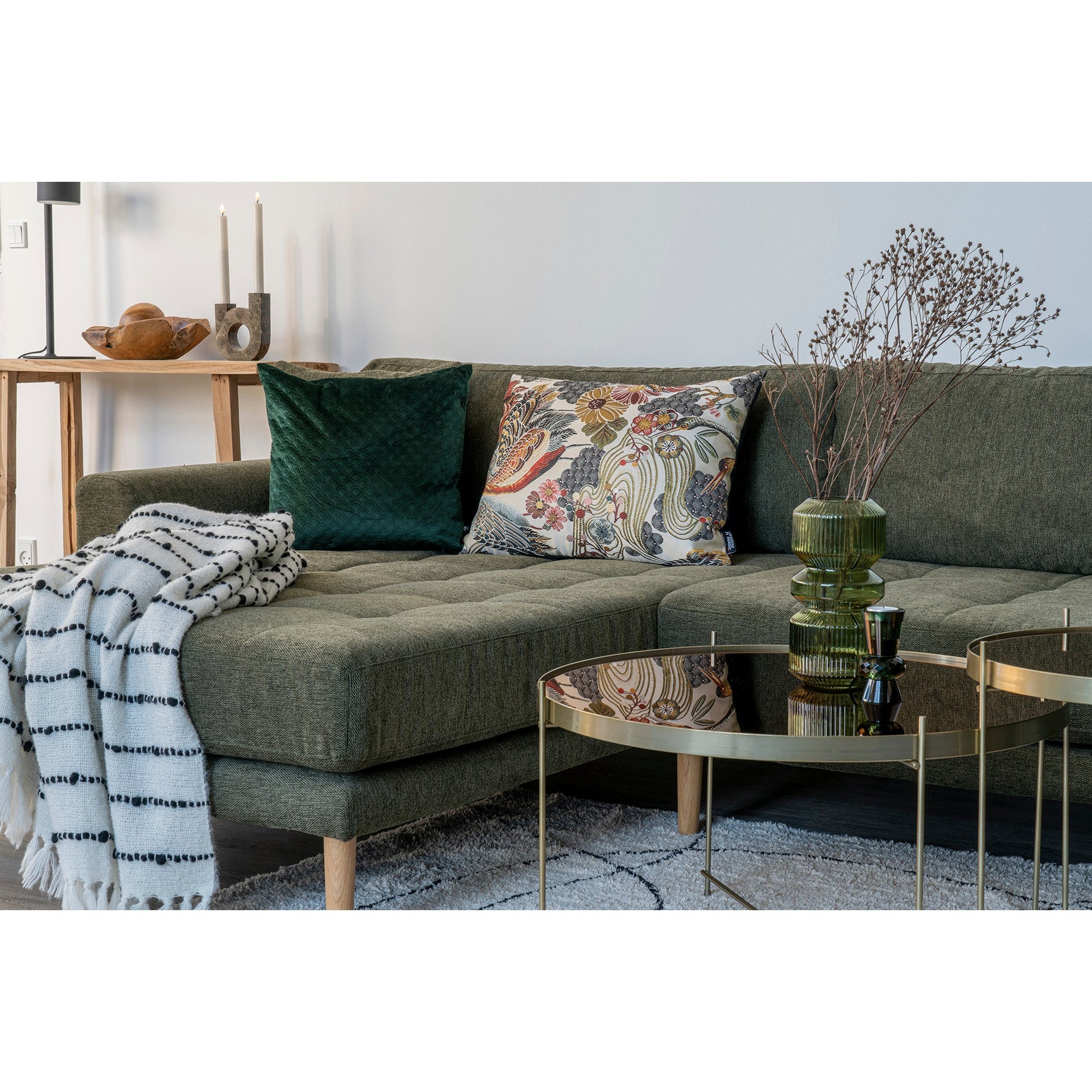 Groene bank met kleurrijke kussens, gestreepte plaid, metalen tafeltjes en decoratieve vaas op tapijt.