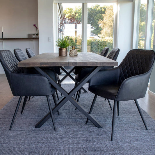 Zwart lederen stoelen en een robuuste houten tafel op een grijskleurig tapijt in een lichte, moderne eetkamer.