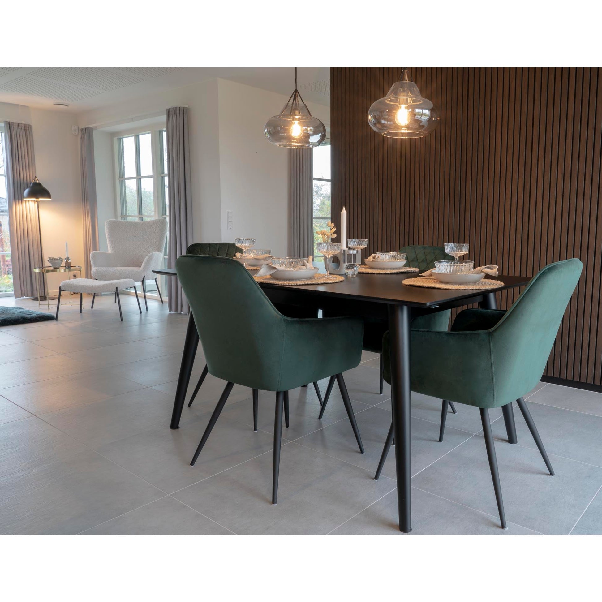 Moderne eetkamer met donkergroen fluwelen stoelen, houten wand en sfeervolle glazen hanglampen.
