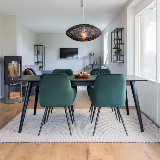 Moderne eetkamer met groene stoelen, zwarte tafel, hanglamp en gezellige haard in lichte, minimalistische stijl.