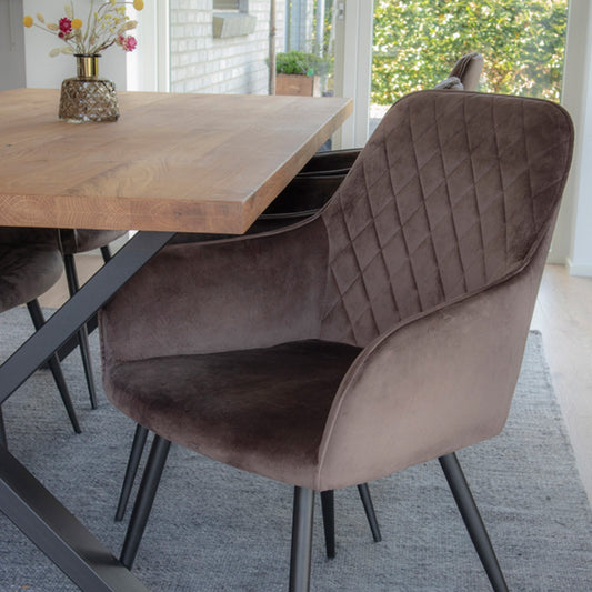 Bruine velvet stoel met ruitpatroon naast houten tafel met vaasje bloemen op grijs tapijt in lichte kamer.