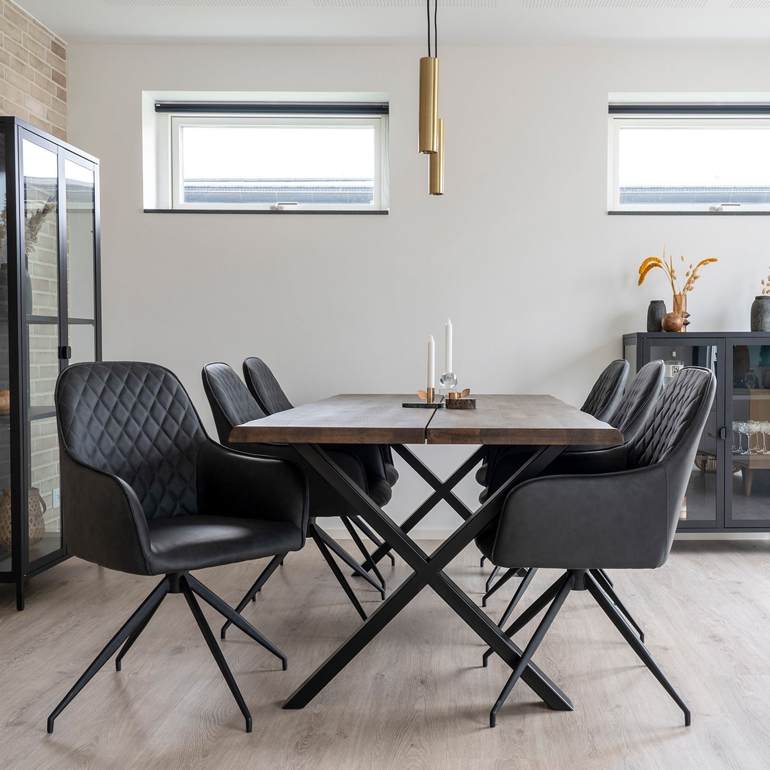 Moderne eetkamer met zwart lederen stoelen, houten tafel, minimalistische decoratie en gouden hanglamp.