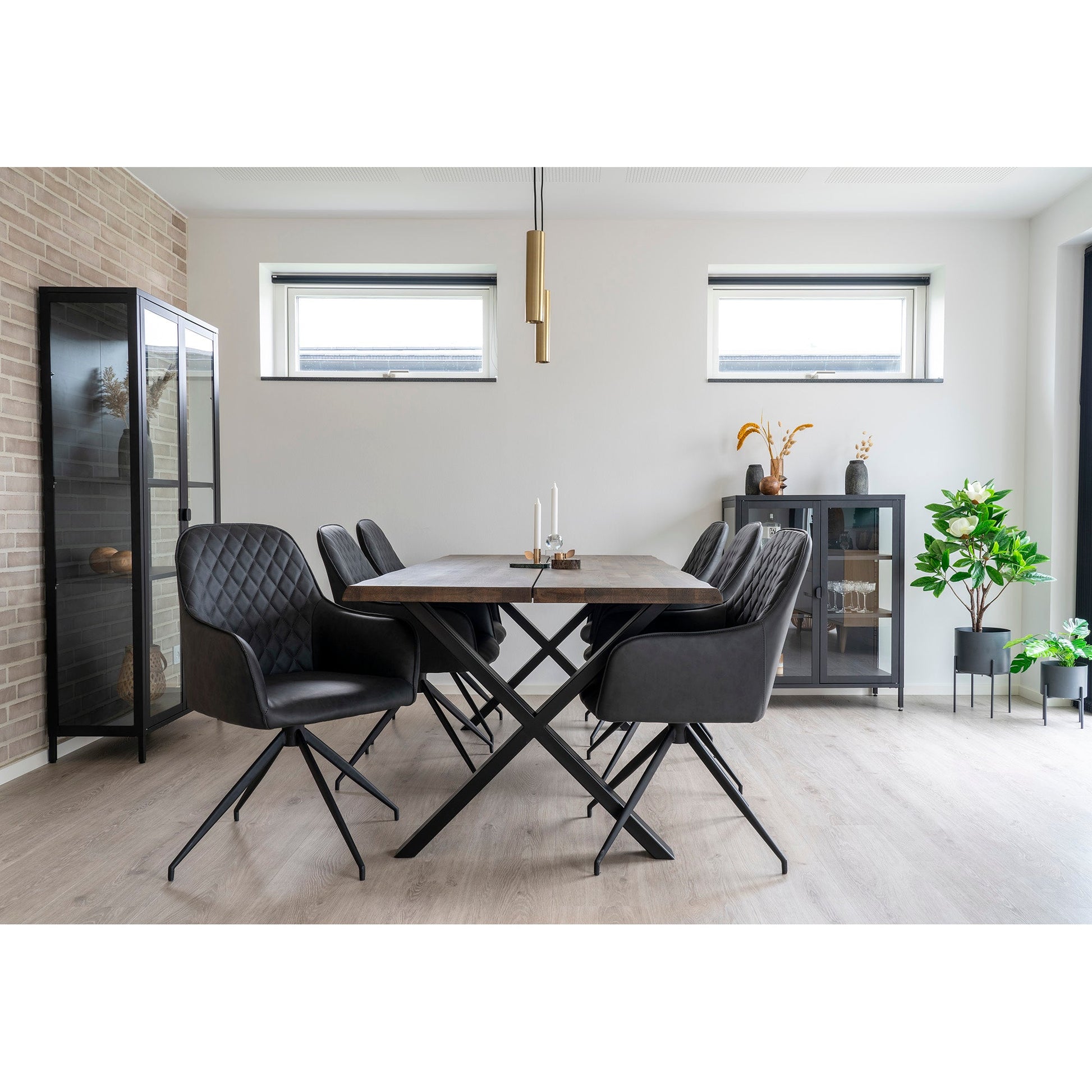Eetkamer met houten tafel, zes zwarte stoelen, glazen kast en groene planten, minimalistische inrichting.