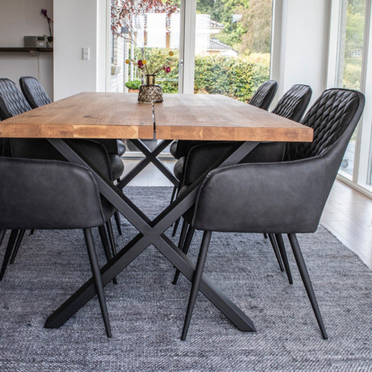 Licht houten eettafel met zwarte metalen poten en zes zwarte lederen stoelen, in een moderne eetkamer.